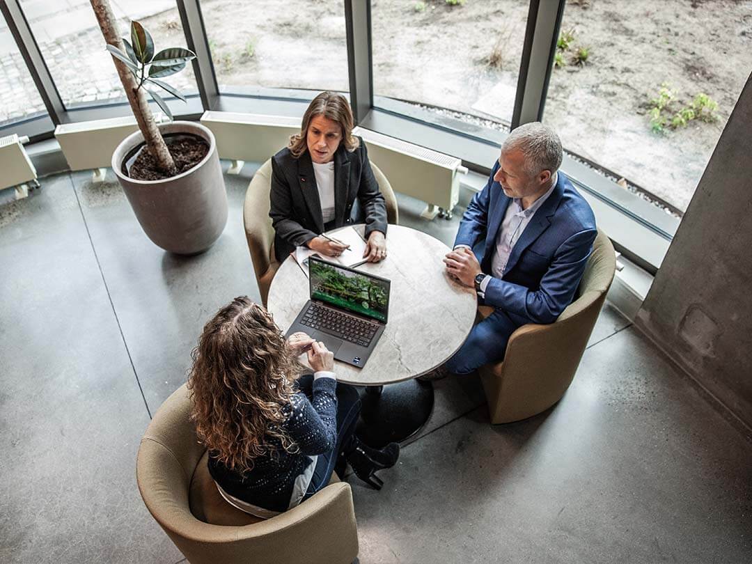 Tre personer sitter rundt et bord og diskuterer