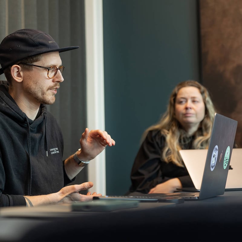 To personer sitter med laptop og snakker sammen